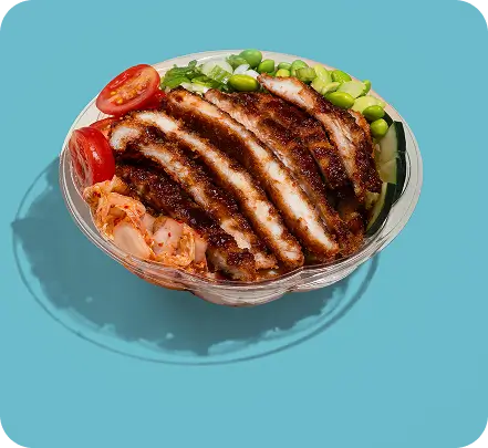 Crispy chicken poke bowl with fresh tomatoes, edamame, and kimchi on a blue background.