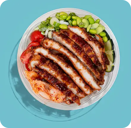 Chicken Katsu bowl with crispy chicken, fresh vegetables, and creamy sauces on a blue background.