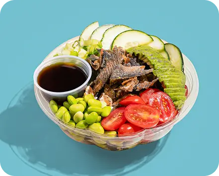 Salmon Skin Salad Bowl with edamame, tomato, avocado, cucumber, and sauce on blue background.