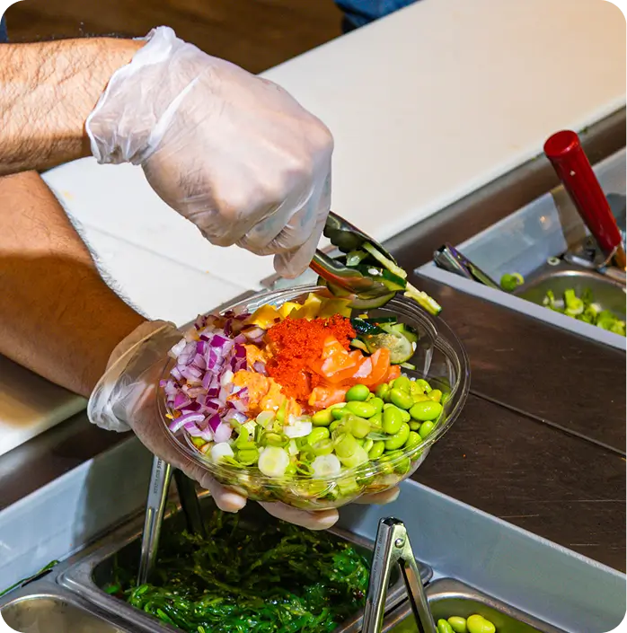 Hawaiian poke bowl with fresh seafood, vibrant veggies, and sauces being prepared at Poke Bowl on Upper East Side.