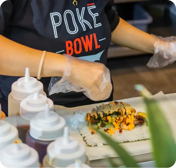Hawaiian-style poke bowl preparation at Long Island City restaurant, showcasing fresh ingredients and sauces.