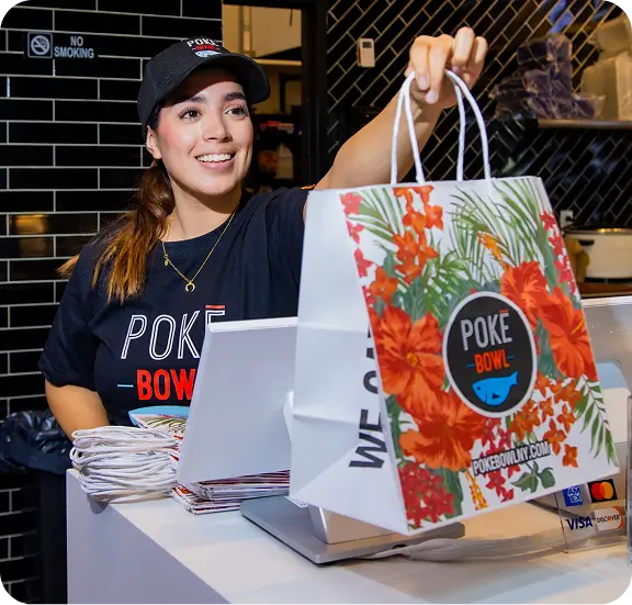 Midtown poke bowl shop staff offering takeout with vibrant, floral-branded bag.