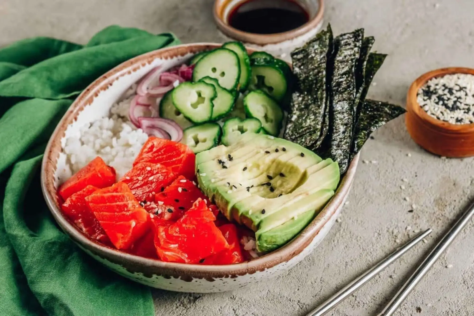 Salmon poke bowl with avocado, cucumber, seaweed, and rice, garnished with black sesame seeds and soy sauce.