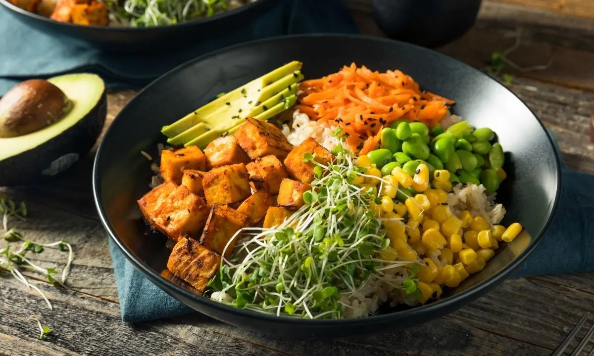 Vibrant vegan poke bowl with tofu, avocado, edamame, corn, and sprouts on rice, highlighting plant-based variety.